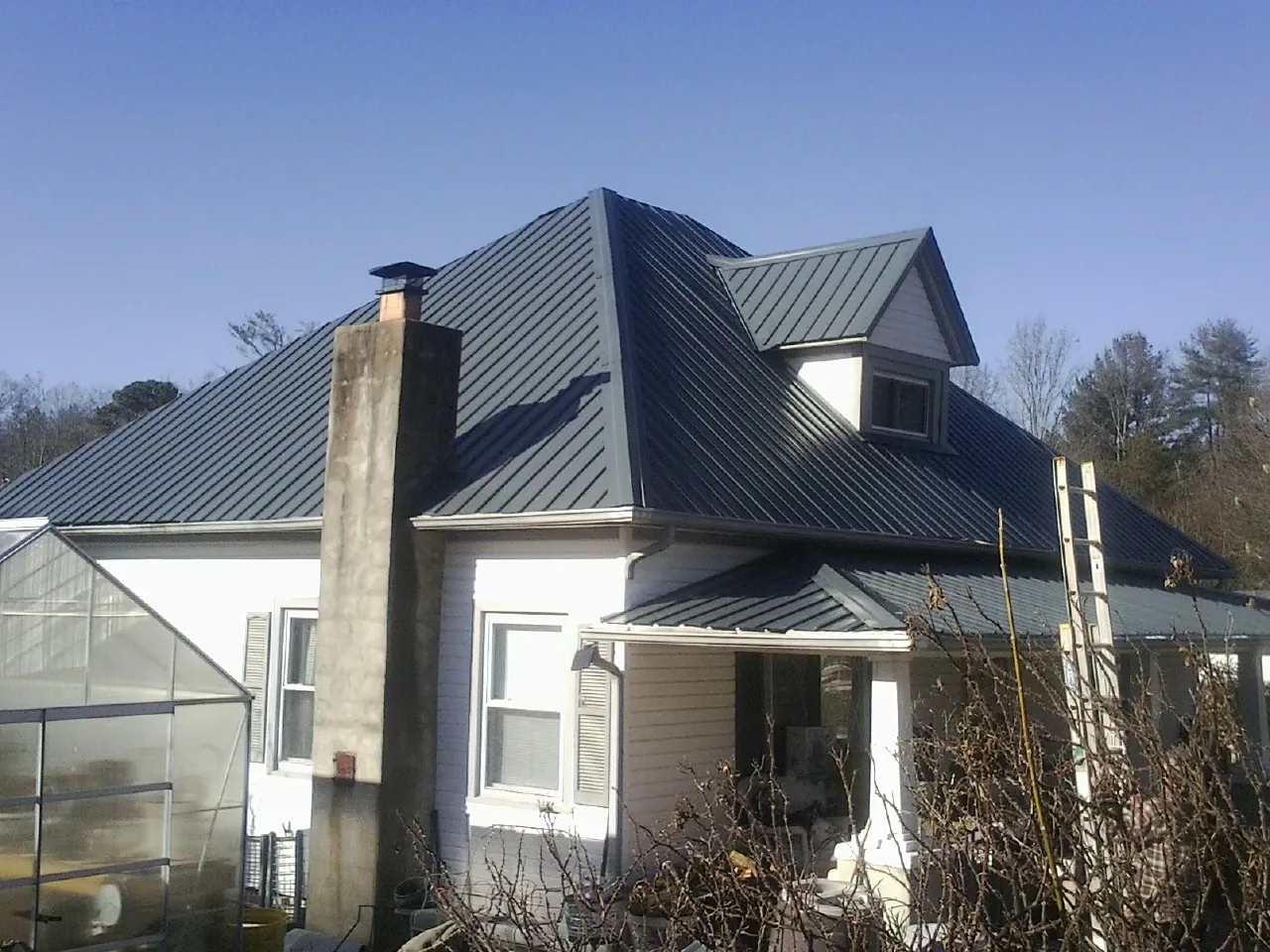 Dark blue standing seam metal roof on a white farmhouse with dormer — Slate & Tile Roof Repair by Roofing Brothers in Corinth