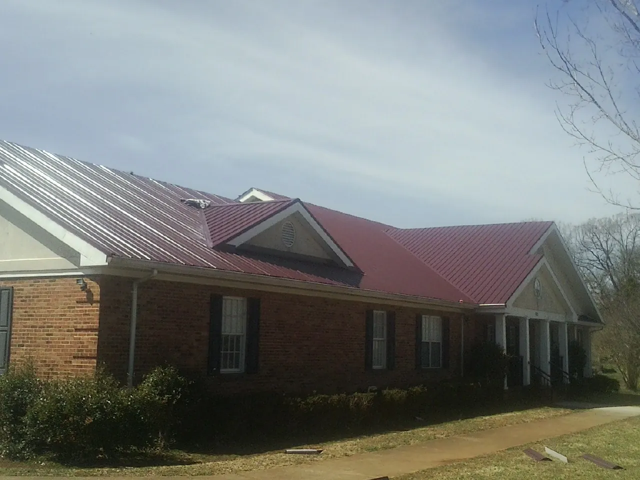 Red metal roof with gabled entries on a long brick building, from a Hail Damage Roof Repair job in Corinth