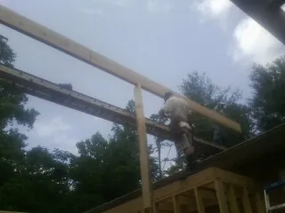 Carpenter setting a ridge beam over a new addition frame in Corinth