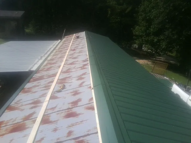 Old rusted panels beside newly installed green metal roofing — Wind Damage Roof Repair by Roofing Brothers in Corinth