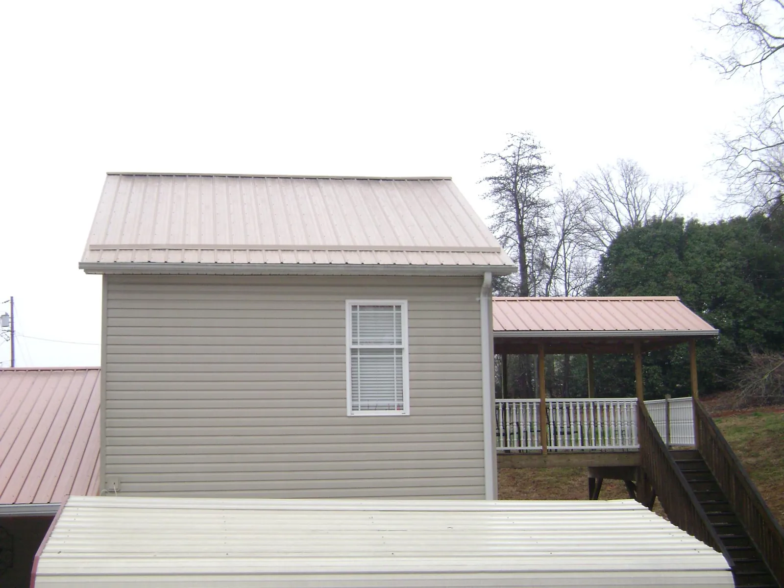 Tan metal roofs on a two story addition and attached porch, from a Roof Replacement job in Corinth